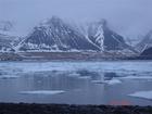 sléttur sjór, hafís, þoka, fjöll með snjó í giljum