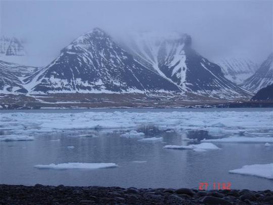 sléttur sjór, hafís, þoka, fjöll með snjó í giljum