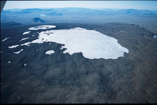 Mynd 2. Okjökul 15. september 2003, horft í suðvestur. Rendur um allan jökulinn sýna að ekki er neitt eftir af ákomusvæði jökulsins og hann því á hröðu undanhaldi. Rákir framan við jökuljaðarinn gefa til kynna hve langt jökullinn náði er hann var hvað stærstur. Að baki gígnum í fjallinu má meðal annars sjá Fanntófell.