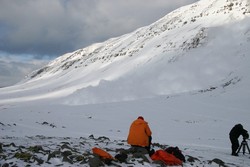 snjókóf í fjallshlíð, tveir menn í forgrunni