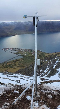 Nýr mælir kominn upp og vakir yfir byggðinni á Flateyri. Til vinstri á mastrinu má sjá bergmálsmælinn. Hægra megin er rafeindabúnaður og leisermælir sem fylgir SM4 mælinum en sjálfur mælirinn er kapal